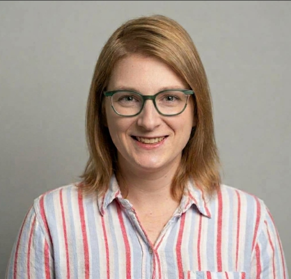 Mallory Long, smiling, wearing green glasses and a striped shirt.